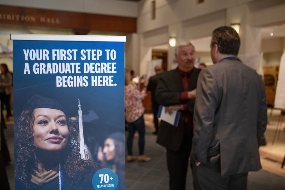 Marketing sign that reads "your first step to a graduate degree begins here" at the graduate showcase.